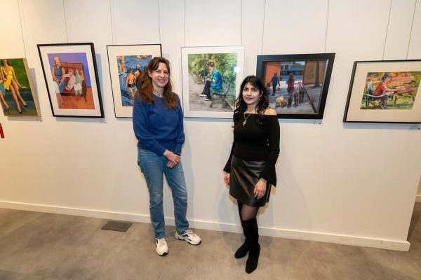 two women standing next to a wall with pictures on it