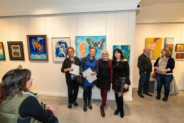 a group of people standing in a room with paintings on the wall